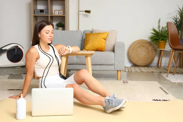 Sporty young woman with jumping rope, fitness tracker and laptop at home