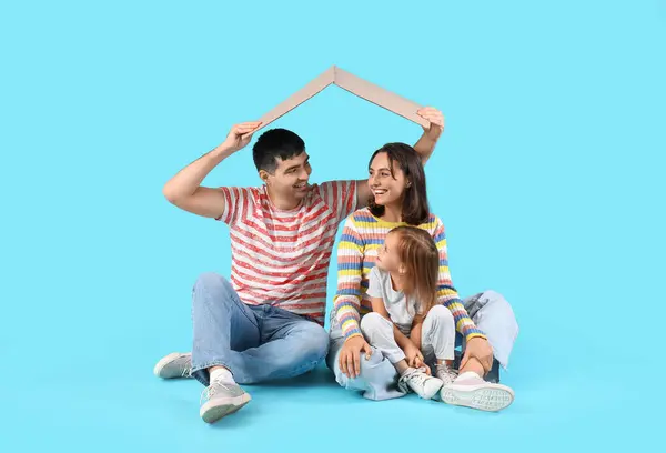 Happy family with cardboard in shape of roof dreaming about their new house on blue background