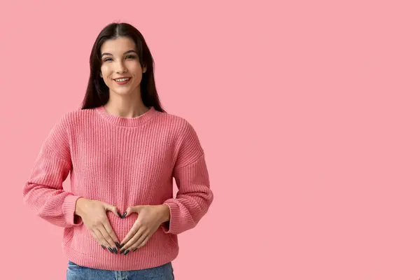 ピンクの背景に彼女の手でハートを作る幸せな妊婦 — ストック写真