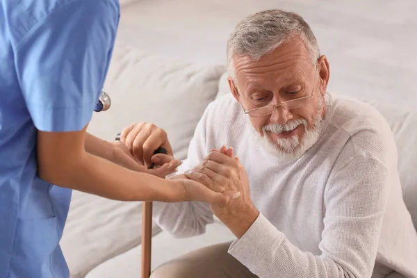 Nurse helping senior man with stick to stand up at home
