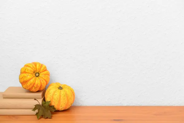 Pumpkins, books and autumn leaves on wooden table near white wall