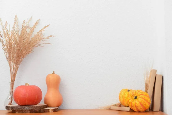 Pumpkins, books and pampas grass on wooden table near white wall