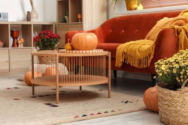 İçinde kahverengi kanepe, ahşap mobilya ve balkabağı olan rahat bir oturma odası.