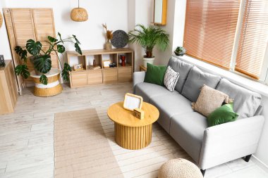 Gri kanepesi, çiçekleri ve ahşap sehpası olan aydınlık oturma odasının içinde.