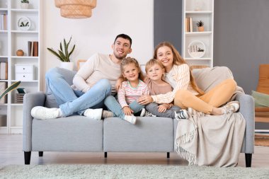 Küçük çocuklar ve aileleri evlerinde kanepede kucaklaşıyorlar.