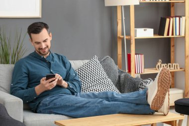 Evdeki koltukta cep telefonu kullanan yakışıklı adam.