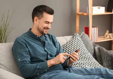 Evdeki koltukta cep telefonu kullanan yakışıklı adam.