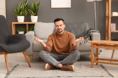 Evde halıda meditasyon yapan yakışıklı bir adam.