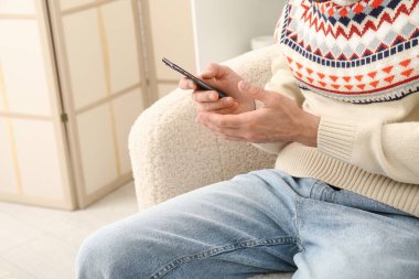 Oturma odasındaki koltukta cep telefonu kullanan yakışıklı adam.