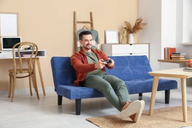 Oturma odasındaki kanepede video oyunu oynayan yakışıklı adam.