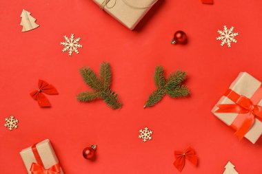 Kırmızı arka planda çam dalları ve hediye kutusu olan Noel kompozisyonu.