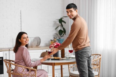 Genç adam kız arkadaşına mutfakta bir bardak şarap veriyor.