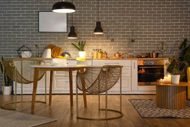 Parlayan lambaları, yemek masası ve akşamları beyaz tezgahları olan modern mutfağın içinde.