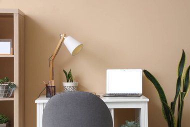 Renk duvarının yanında modern dizüstü bilgisayarı ve lambası olan rahat bir iş yeri