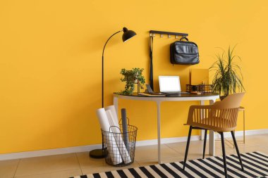 Modern dizüstü bilgisayarı ve sarı duvarın yanında bitkileri olan şık bir iş yeri.