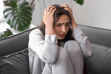 Oturma odasındaki kanepede oturan güzel, genç, korkak kadın.