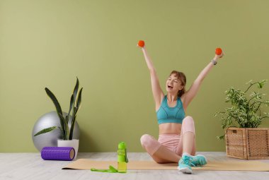 Genç ve sportif kadın evde dambıllarla antrenman yapıyor.