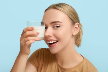 Mavi arka planda bir bardak sütü olan güzel genç bir kadın.