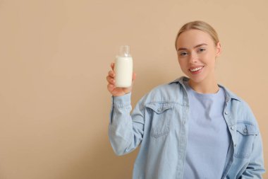 Bej arka planda cam süt şişesi olan güzel genç bir kadın.
