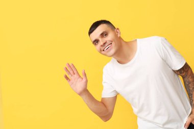 Sarı arka planda el sallayan yakışıklı genç adam.