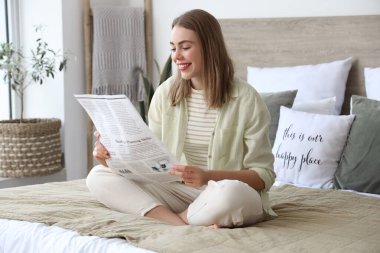 Evdeki yatak odasında gazete okuyan güzel genç bir kadın.