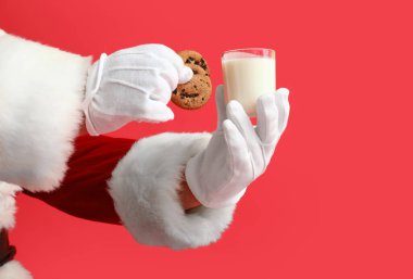 Kırmızı arka planda bir bardak süt ve kurabiyeli Noel Baba