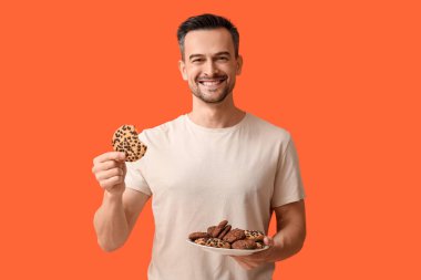 Turuncu arka planda bir tabak lezzetli kurabiyesi olan yakışıklı adam.