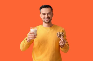 Lezzetli kurabiyesi ve turuncu arka planda bir bardak sütü olan yakışıklı adam.