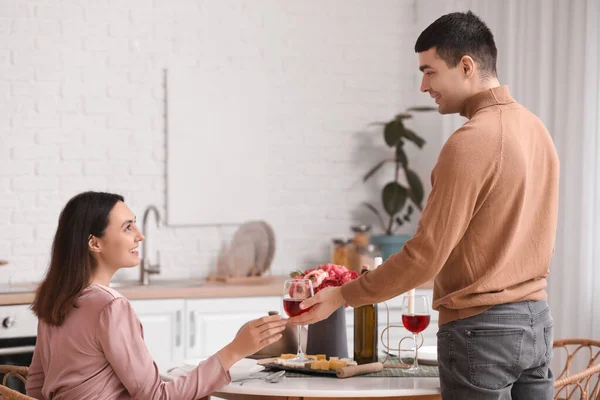 Young man giving his girlfriend glass of wine in kitchen