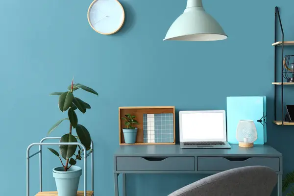 Stylish workplace with modern laptop, stationery and lamp near color wall