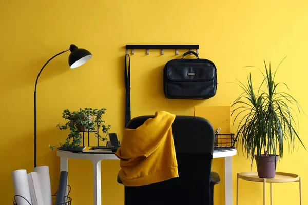 Stylish workplace with briefcase and houseplants near yellow wall