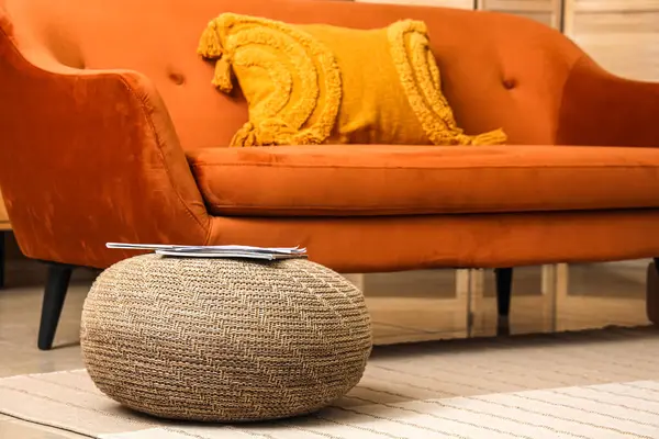 Wicker pouf with magazine and orange sofa in living room, closeup