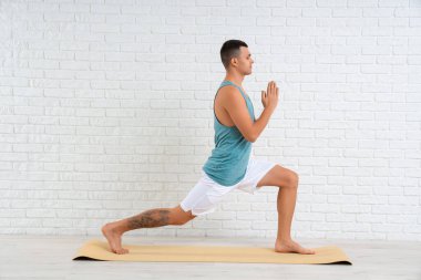 Beyaz tuğla duvarın yanında yoga yapan genç bir adam.