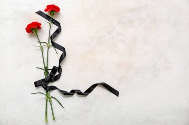 Karanfiller açık arkaplanda siyah cenaze kurdelesiyle bağlanmış.