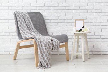 Boş cenaze çerçeveli masa, yanan mum ve ışıklı tuğla duvarın yanındaki sandalye.