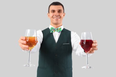 Gri arka planda şarap kadehleri olan genç barmen.