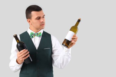 Gri arka planda şarap şişeleri olan genç barmen.