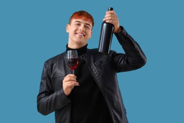 Mavi arka planda şişe ve bir bardak şarap olan genç adam.