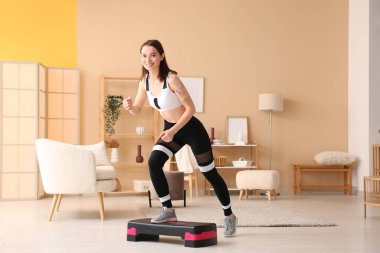 Spor yapan genç bir kadın. Adımlarıyla evde egzersiz yapıyor.