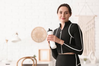 Evde su şişesi olan genç bir kadın.