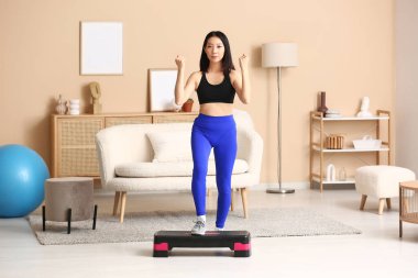 Sportif, genç Asyalı bir kadın. Adımlarıyla evde egzersiz yapıyor.