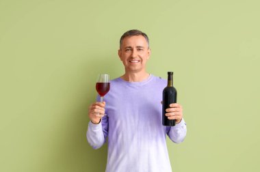 Yeşil arka planda cam ve kırmızı şarap şişesi olan olgun bir adam.