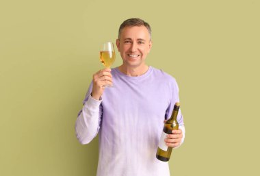 Yeşil arka planda cam ve şarap şişesi olan olgun bir adam.