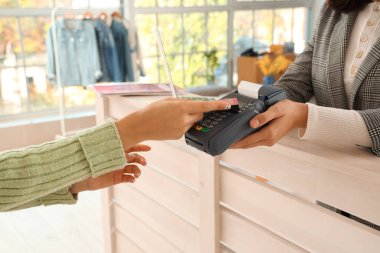 Kadın satıcı giyim mağazasında müşteriden ödeme alıyor, yakın plan.