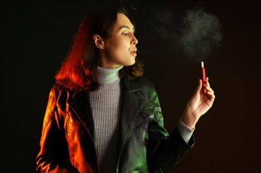 Güzel genç bir kadın, arka planda elektronik puro içiyor.