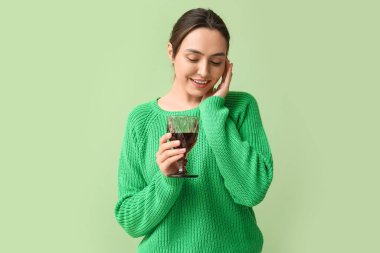 Yeşil arka planda kırmızı şarap kadehi olan güzel genç bir kadın.