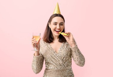 Parti şapkalı güzel bir kadın, bir bardak beyaz şarap ve pembe arka planda ıslık çalıyor.