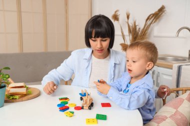Genç anne ve küçük oğlu mutfaktaki masada yapı taşlarıyla oynuyorlar.