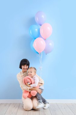 Genç anne ve küçük oğlu mavi duvarın yanında oyuncak tavşancığı var.
