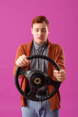 Mor arka planda direksiyon simidi olan endişeli genç adam.